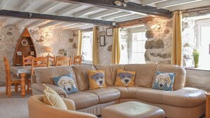 Ein gemütliches Wohnzimmer mit einem großen L-förmigen Sofa, einem kleinen runden Hocker und einem Holzespeisetisch mit Stühlen.