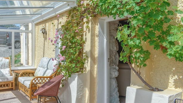 Eine sonnendurchflutete Terrasse mit Korbmöbeln, einer Kletterpflanze und einer Steinmauer.