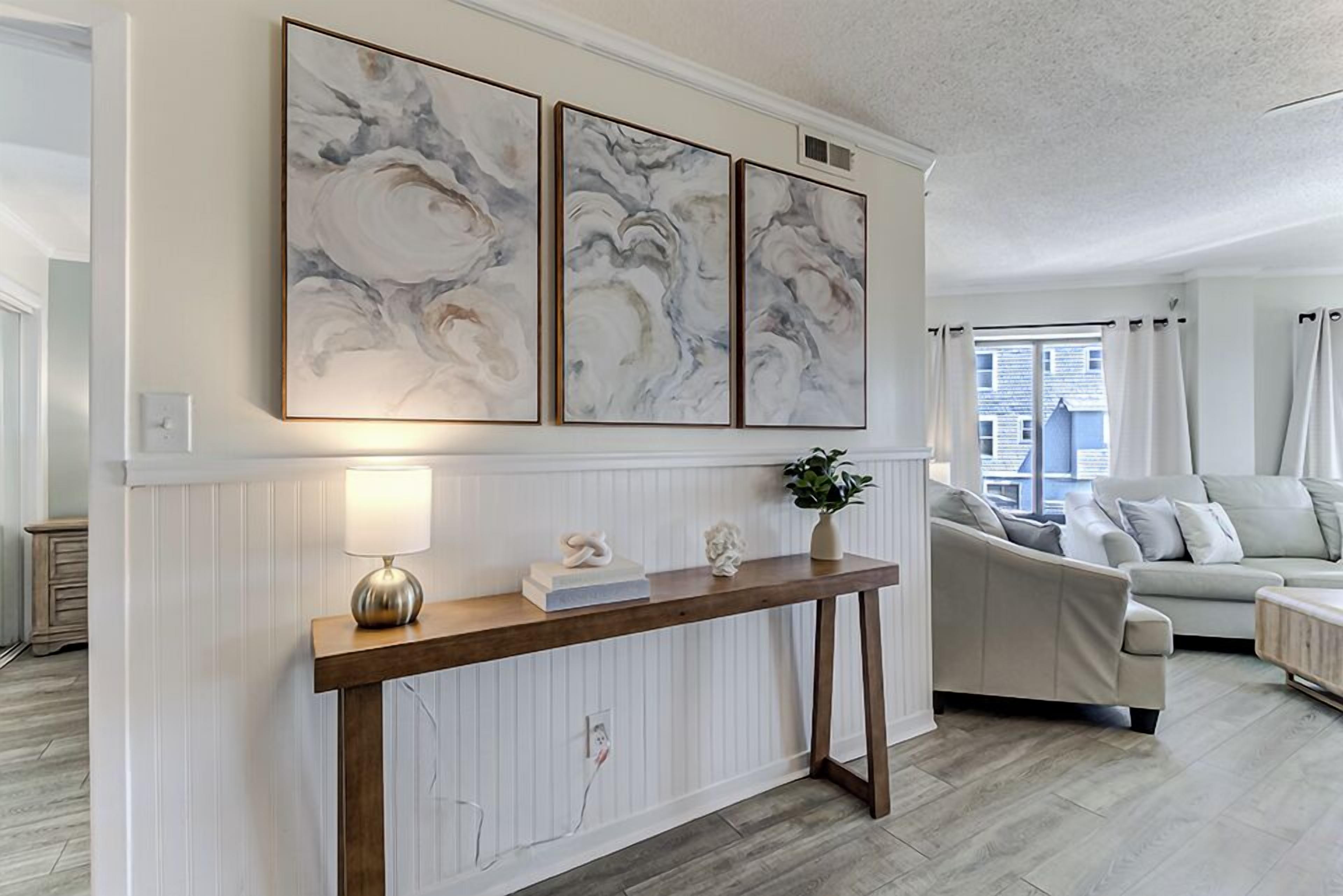 Un salon avec une console en bois, une lampe et trois tableaux abstraits accrochés au mur.