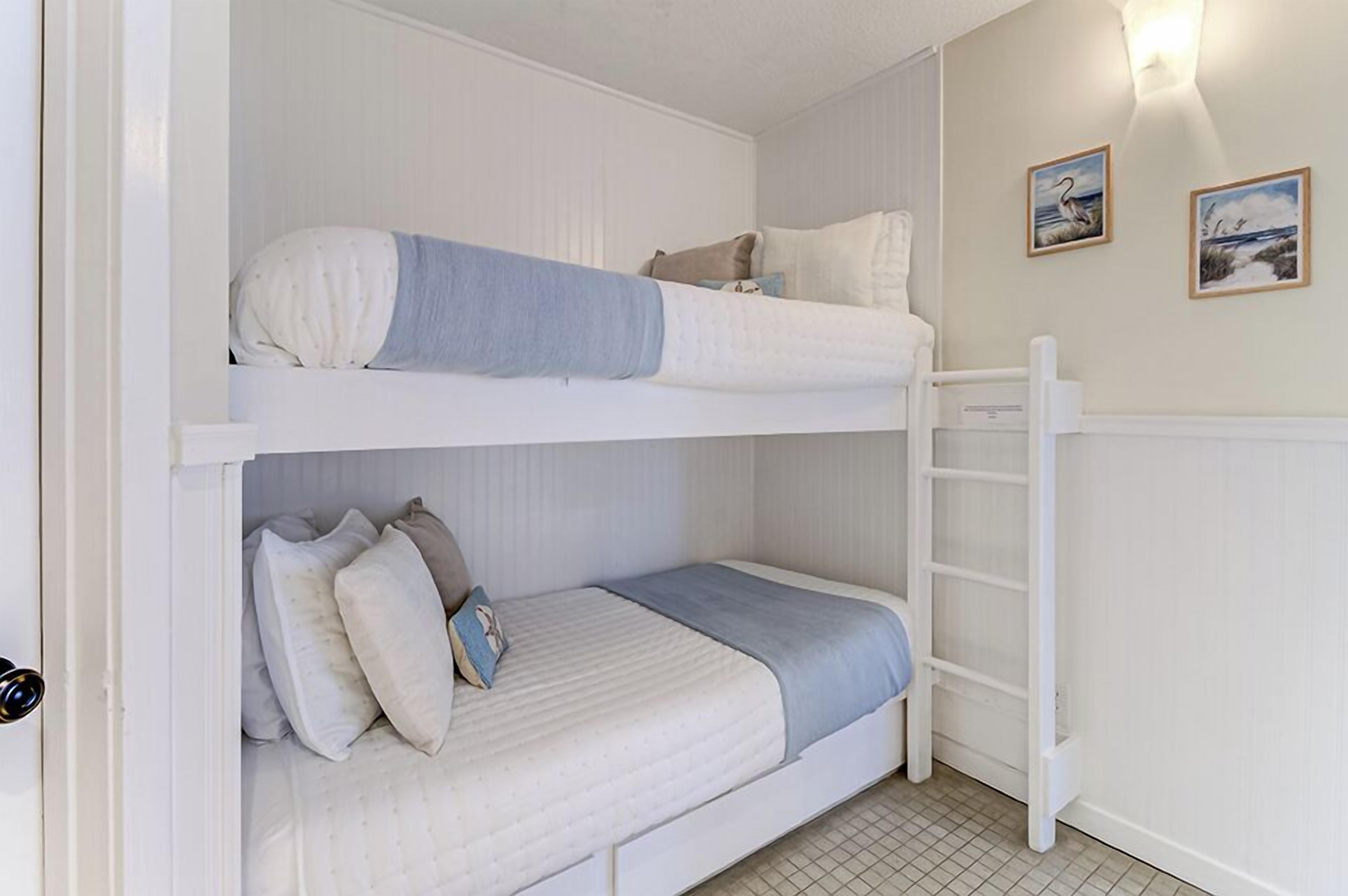 A bunk bed room with a ladder, two framed pictures on the wall, and a tiled floor.