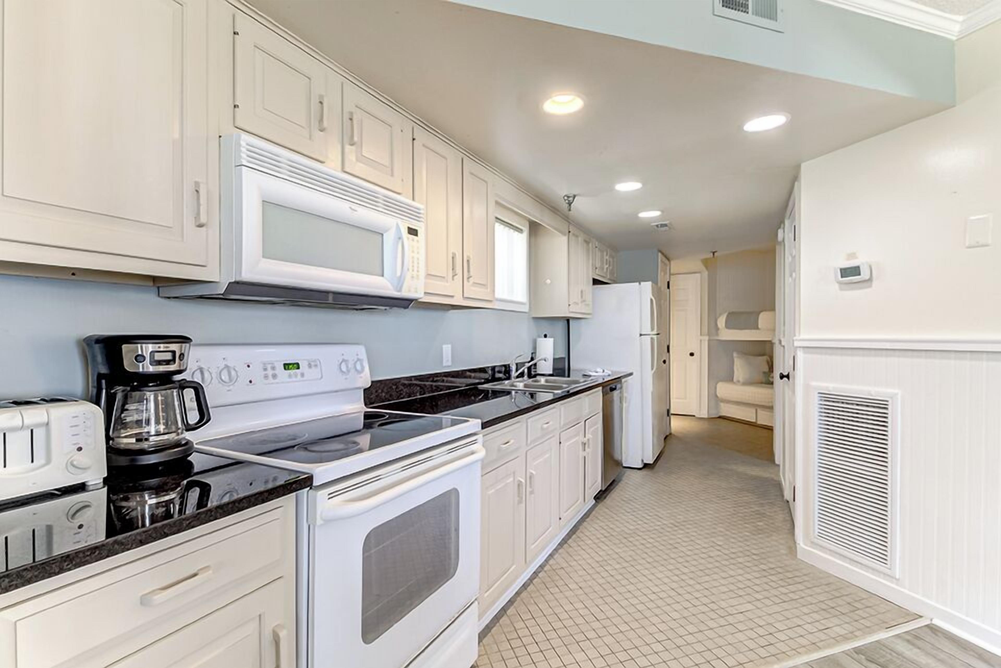 A modern kitchen with white cabinets, a black countertop, a microwave, a coffee maker, and a refrigerator.