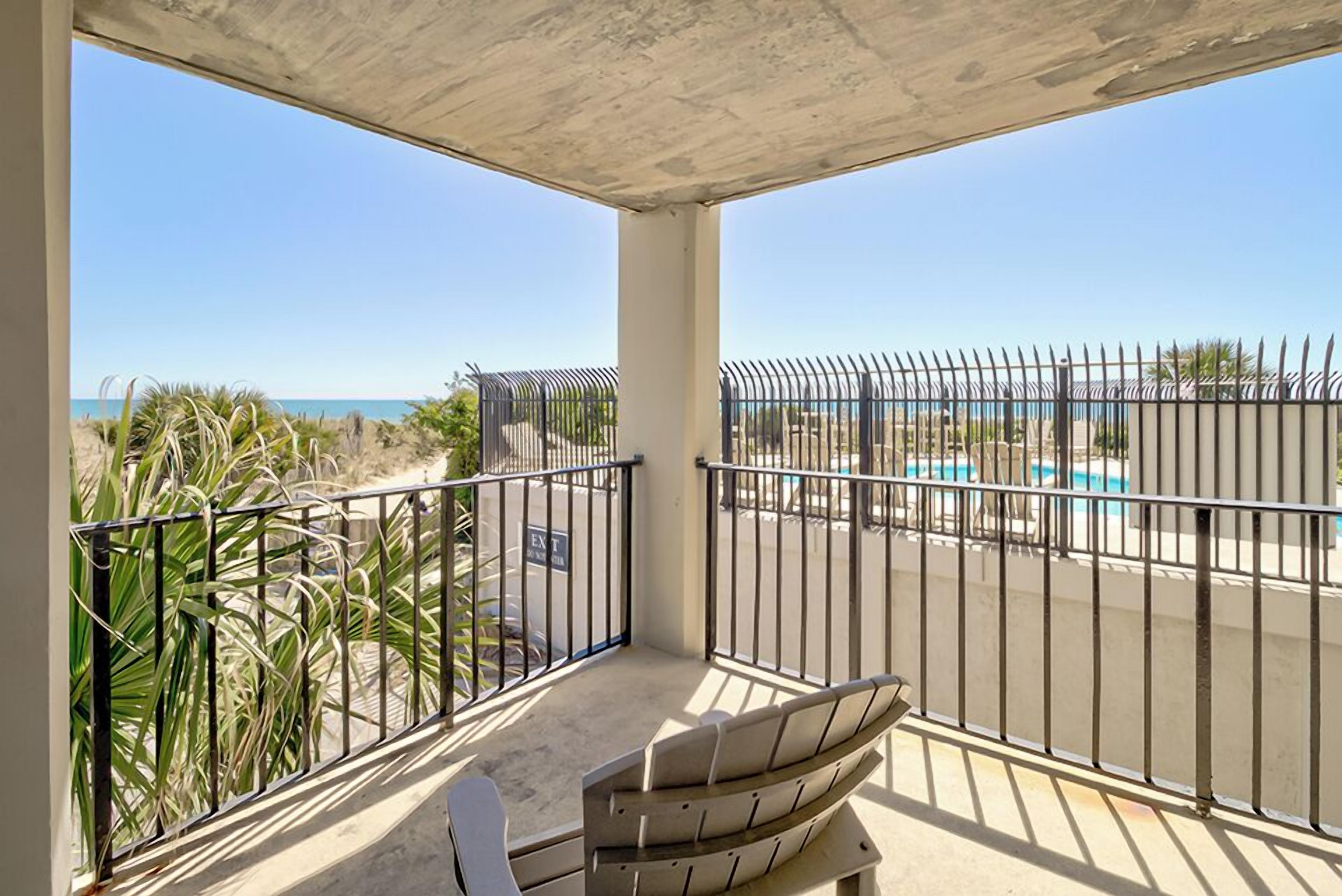 A balcony with a view of the beach and a pool.