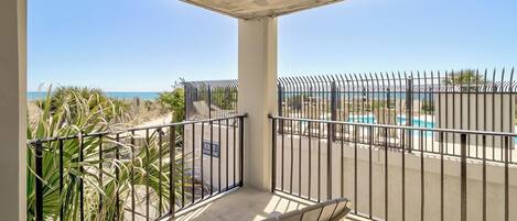 A balcony with a view of the beach and a pool.