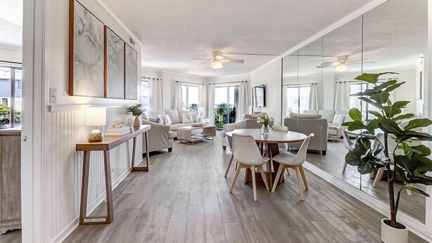 A spacious living area with a dining table, sofas, and a large mirror reflecting the room. - Oceanfront Balcony Views, Pool, STEPS to Beach Restaurants Shops (Wrightsville Beach)