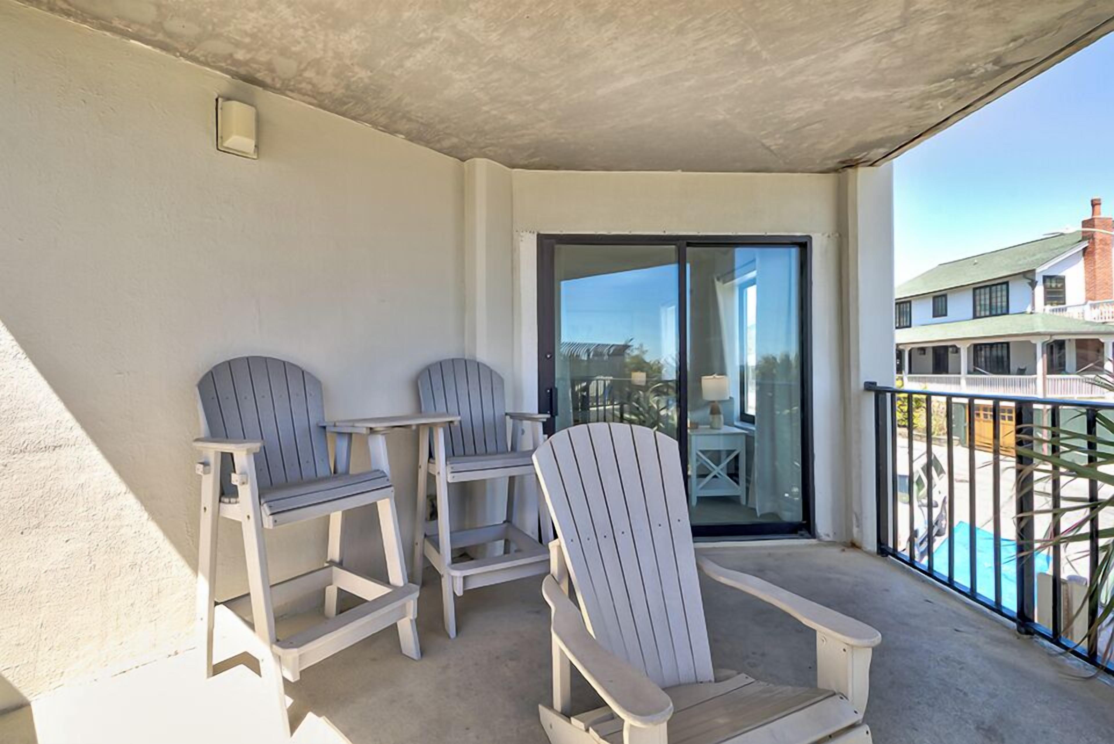 Uma varanda com duas cadeiras Adirondack, uma porta de vidro e vista para um edifício e uma piscina.
