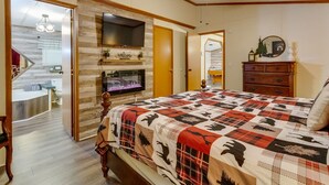 Een slaapkamer met een groot bed, een aan de muur bevestigde televisie, een open haard en een houten deur naar een badkamer.