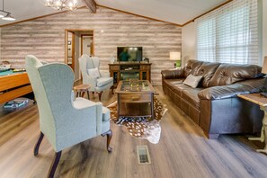 A cozy living room with a wooden wall, a leather sofa, a coffee table, and a television. - Spacious 3Bed/2Bath home just 1 mile off exit 407 (Kodak)