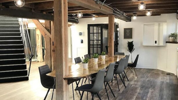 A modern dining area with a long wooden table, black chairs, and potted plants.