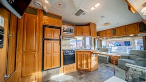 A compact RV kitchen with wooden cabinets, a stove, microwave, and a refrigerator. - Minigolf Course TIGER Camper Hot Tub - AC - Furnace - Fully Furnished (St. Regis)