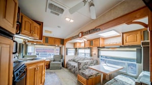 A compact RV kitchen with wooden cabinets, a stove, and a dining area with a table and cushioned seating. - Minigolf Course TIGER Camper Hot Tub - AC - Furnace - Fully Furnished (St. Regis)