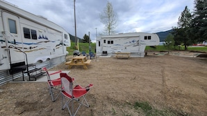 A campsite with two RVs, picnic tables, and a red folding chair. - Minigolf Course TIGER Camper Hot Tub - AC - Furnace - Fully Furnished (St. Regis)