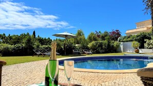 Zona piscina con un tavolo apparecchiato per due, una bottiglia di champagne e un bicchiere.