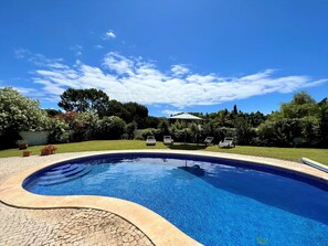 Une piscine dont le bord est revêtu de carrelage, entourée d’une pelouse et d’arbres.