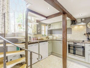 A kitchen with a wooden staircase, white cabinets, a stainless steel oven, and a globe on the window sill.