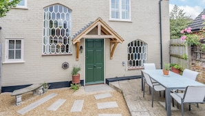 Ein charmantes Haus mit grüner Tür, zwei Fenstern mit Dekorationsglas, einer hölzernen Bank und einem Tisch mit Stühlen im Garten.