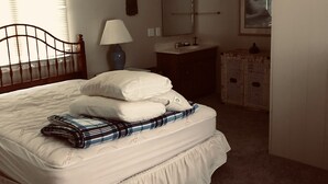 Un dormitorio con cama, ventilador de techo, mesita de noche, espejo y ventana con persianas.