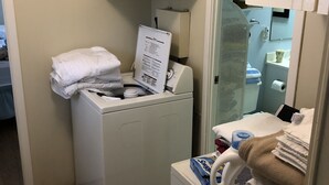 Un lavadero pequeño con lavadora y secadora frontales, un armario pequeño sobre la secadora, y un espejo que refleja el área del baño.