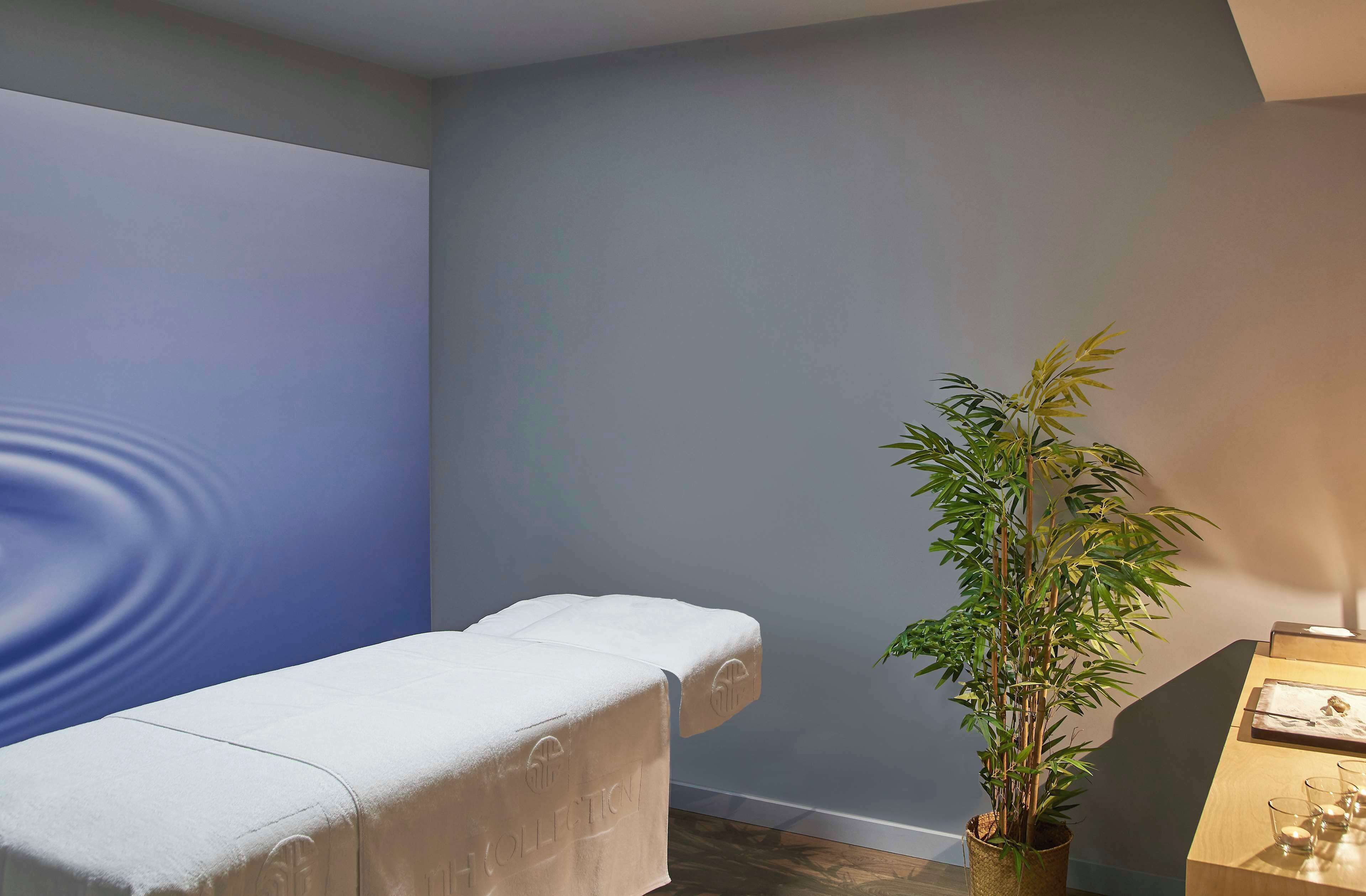 A room with a massage table, a potted plant, and a small table with glasses and a candle.