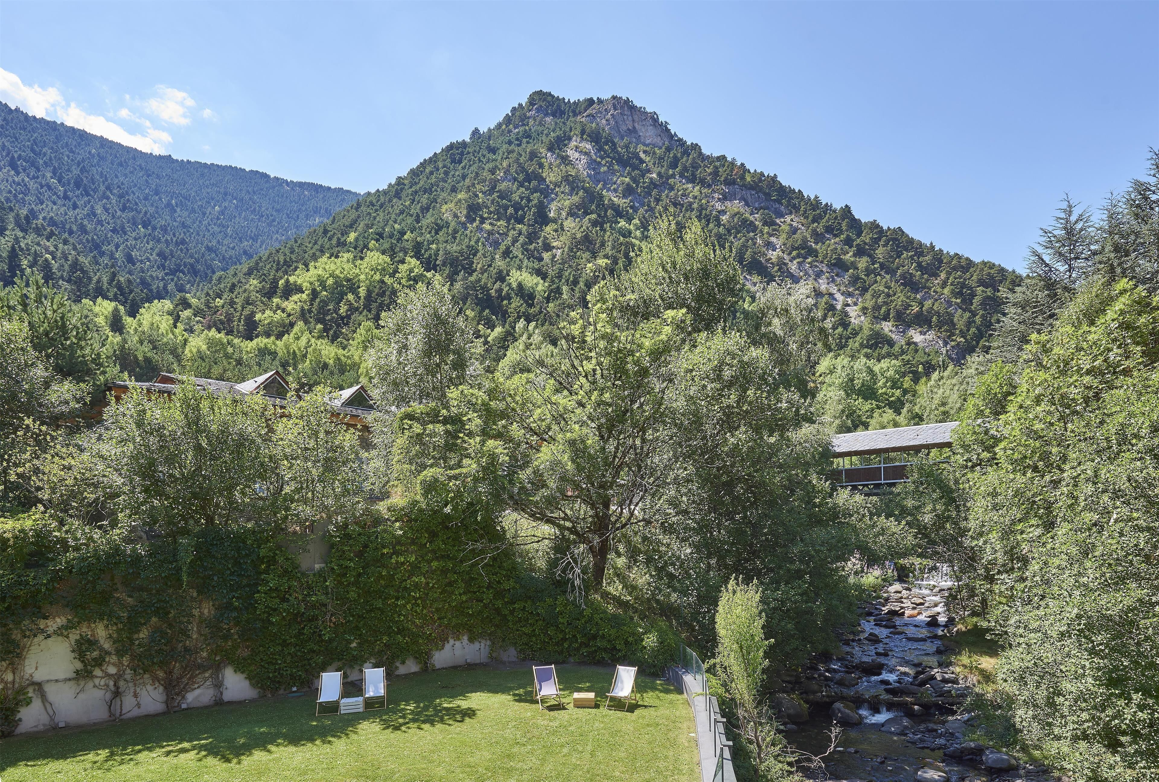 A mountain view with a grassy area, two lounge chairs, and a building in the foreground.