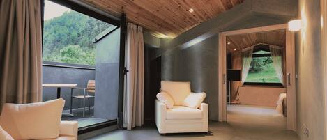 A modern room with a wooden ceiling, a white sofa, a chair, and a view of a forest through large windows.
