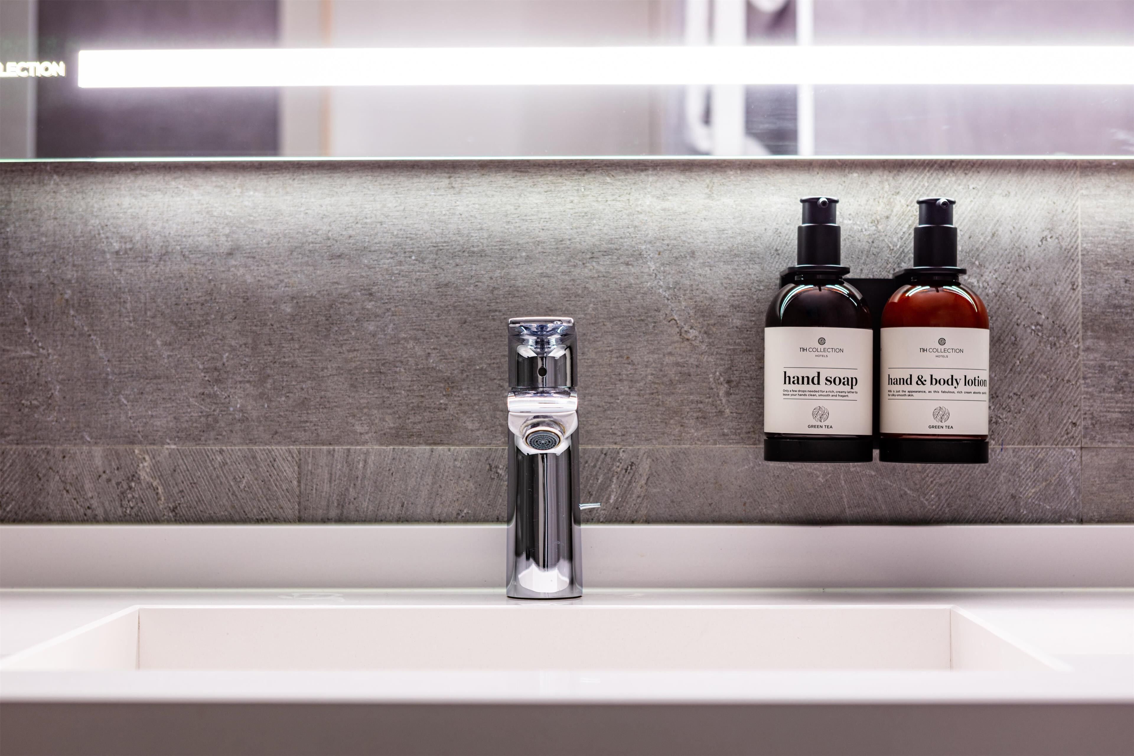 A bathroom with a modern faucet and two bottles of hand soap and body lotion on the wall.