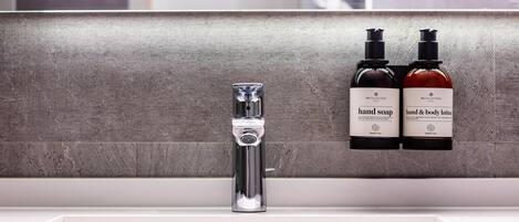 A bathroom with a modern faucet and two bottles of hand soap and body lotion on the wall.
