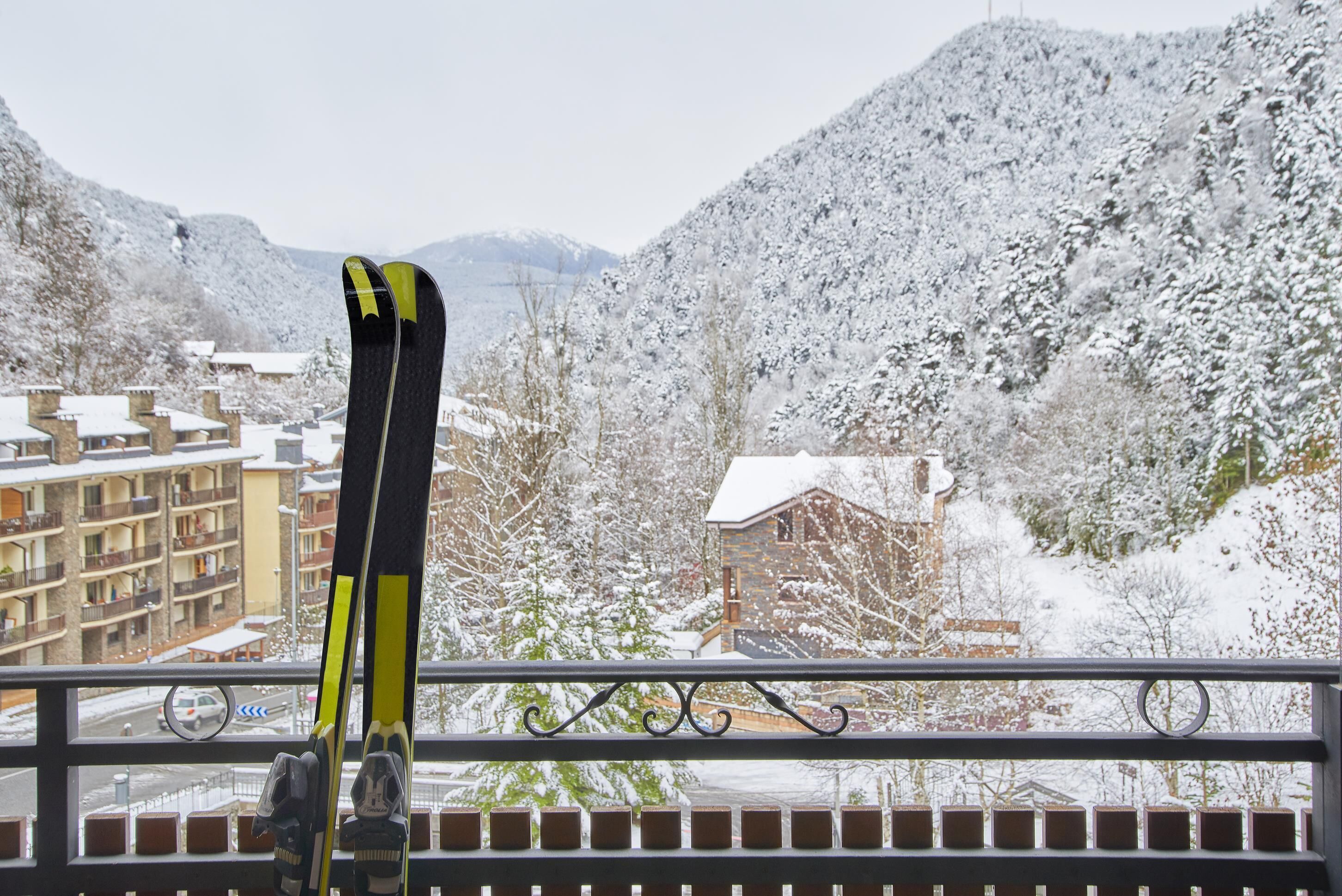 A pair of skis leaning against a balcony railing overlooking a snowy mountain landscape with buildings.