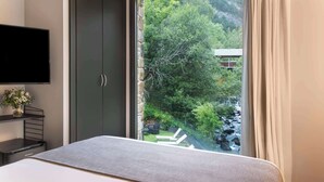 A bedroom with a bed, a TV, a wardrobe, and a window with a view of greenery and a building. - NH Collection Andorra Palome (Arinsal)