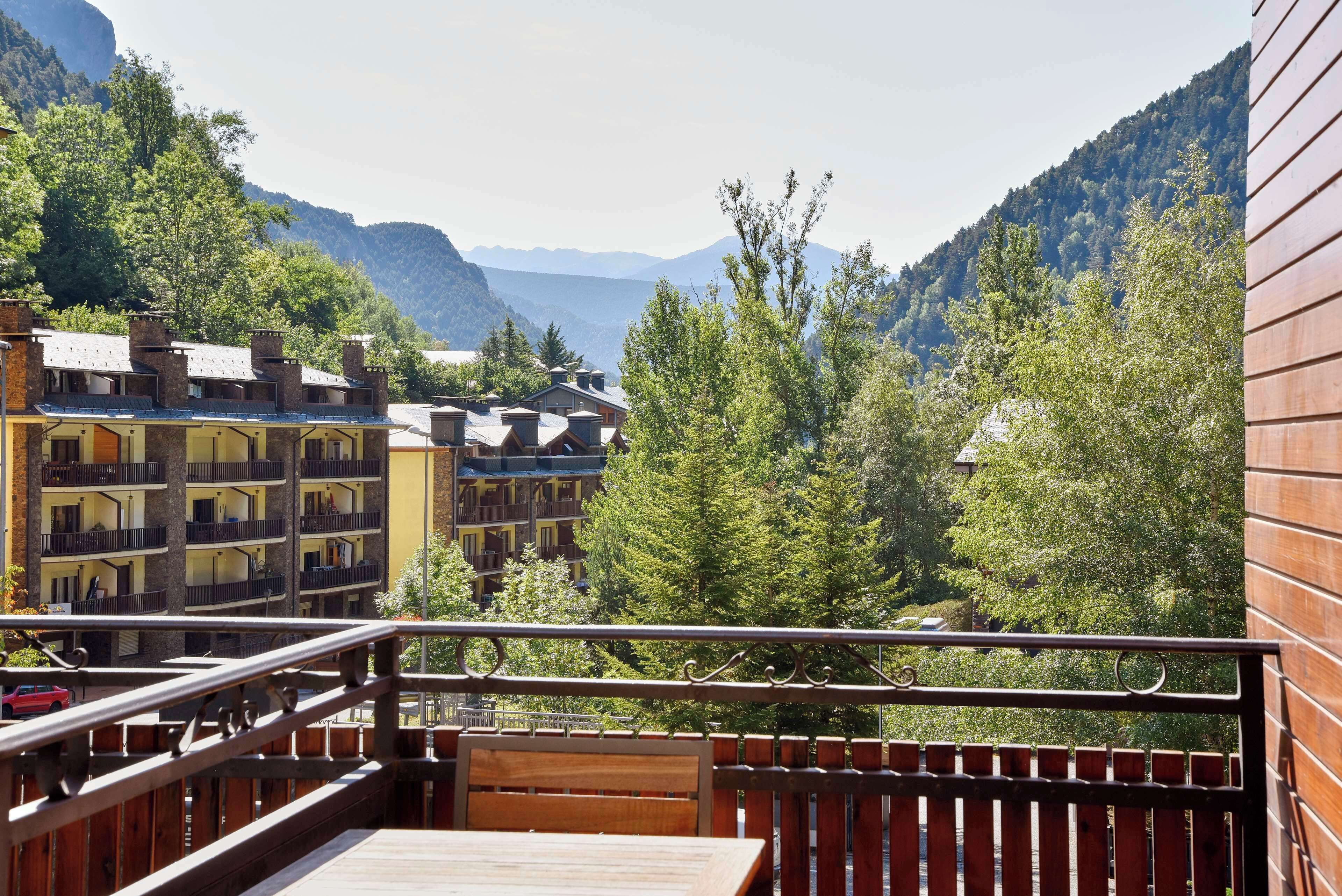 A balcony with a wooden railing overlooking a mountainous area with buildings and trees.