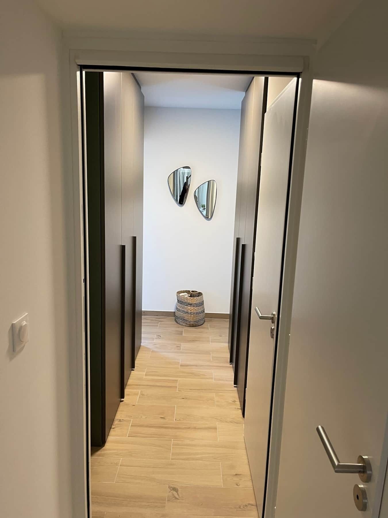 Un pasillo con suelo de madera, una cesta en el suelo y dos espejos colgados en la pared.