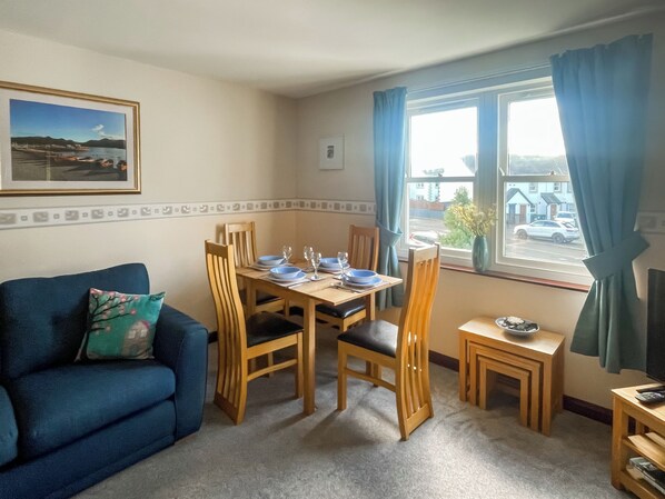 A dining area with a table set for four, a blue sofa, and a window with curtains. - 14 Elm Court, Elliott Park (Keswick)
