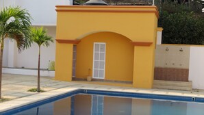 A small, yellow building with a door and a window, adjacent to a swimming pool. - BONADAY HOTEL (Ometepec)