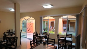 A dining area with tables and chairs, large arched windows, and a view of the outdoor patio. - BONADAY HOTEL (Ometepec)