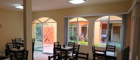 A dining area with tables and chairs, large arched windows, and a view of the outdoor patio.