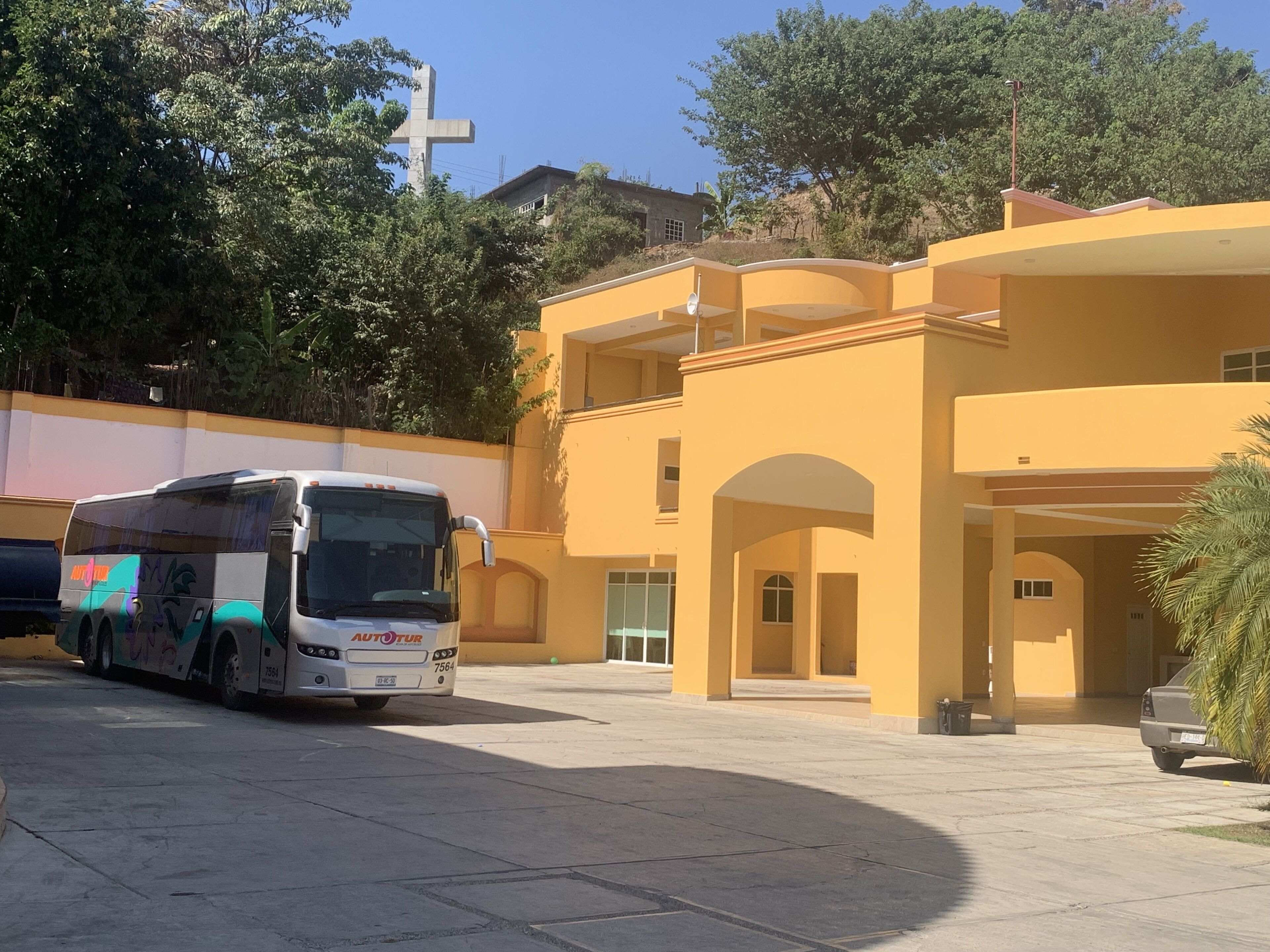 A bus parked in front of a yellow building with a cross in the background.