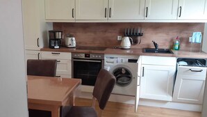 Een compacte keuken met witte kastjes, een koffiezetapparaat, een broodrooster, een oven, een wasmachine en een vaatwasser.