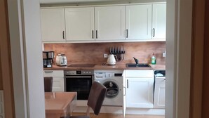 Een kleine keuken met witte kastjes, een koffiezetapparaat, een broodrooster en een wasmachine.