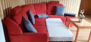 Un sofá seccional rojo con un reposapiés a juego y una pequeña mesita de madera con una planta.