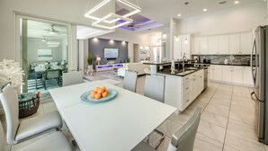 Une cuisine moderne avec des meubles blancs, un îlot central et un coin repas comprenant une table et des chaises blanches.