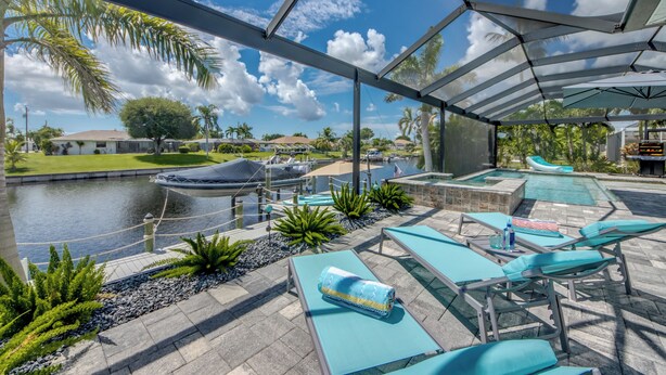 Un espace extérieur abrité, doté de chaises longues et d’une piscine, offrant une vue sur un plan d’eau et une marina.