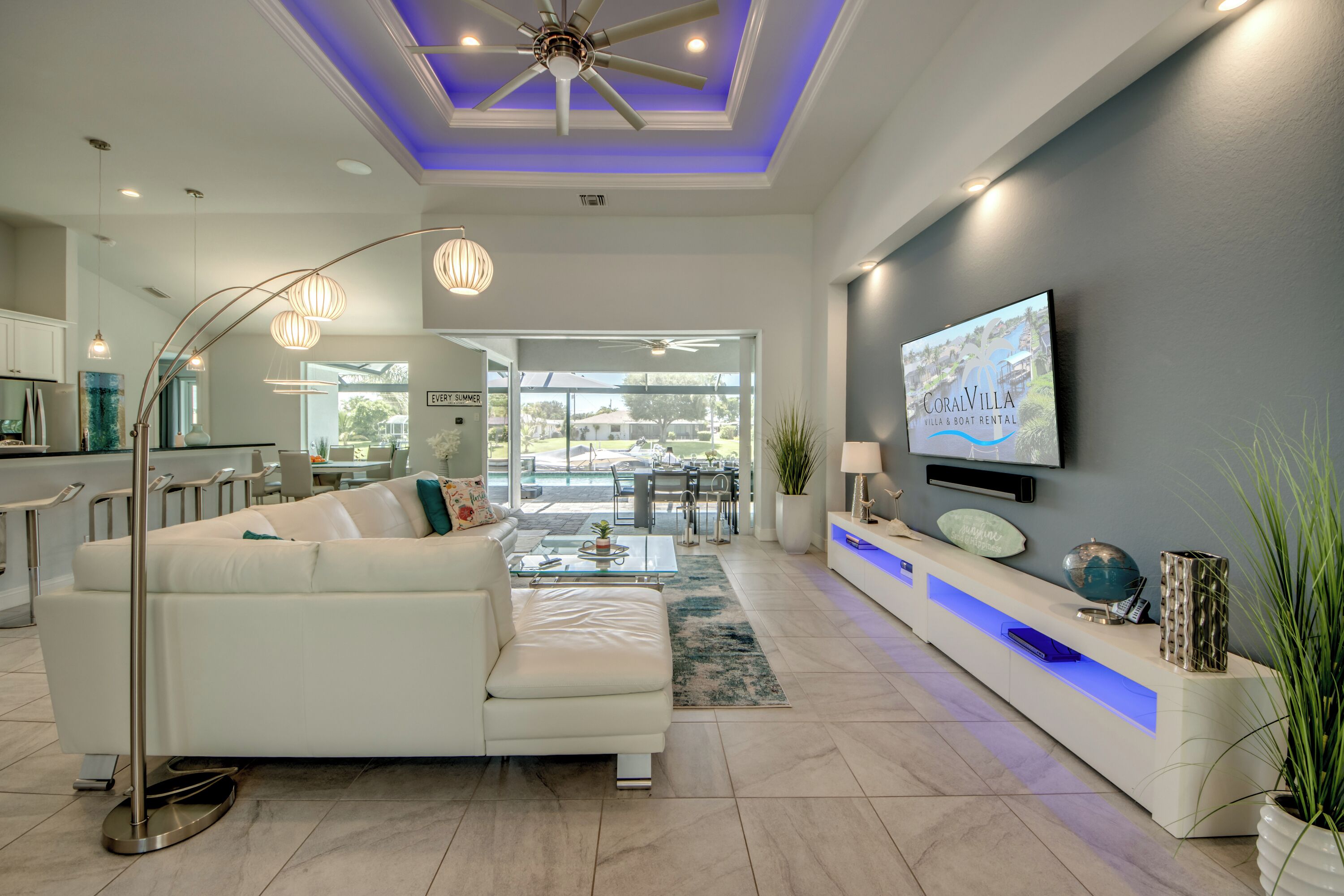 A modern living room with a white sofa, a glass coffee table, and a TV mounted on a grey wall.
