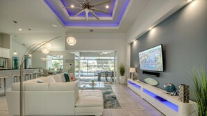 Un salon moderne avec un canapé blanc, un ventilateur de plafond, un téléviseur fixé au mur et un comptoir d’accueil.
