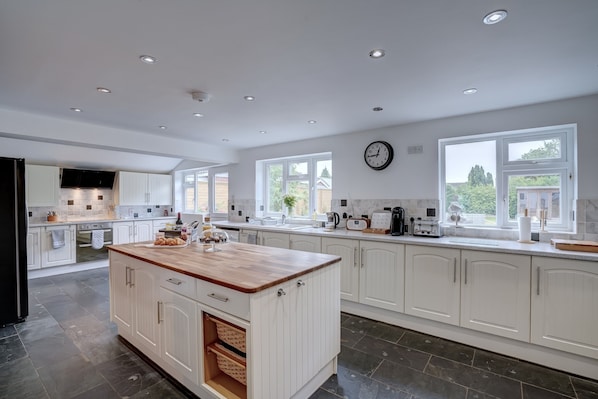 A spacious kitchen with white cabinetry, a wooden island, and a large window providing natural light.