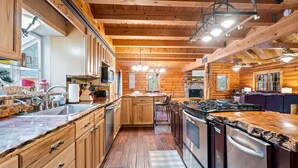 A log cabin-style kitchen with wooden cabinets, a central island, stainless steel appliances, and a dining area with a table and chairs.