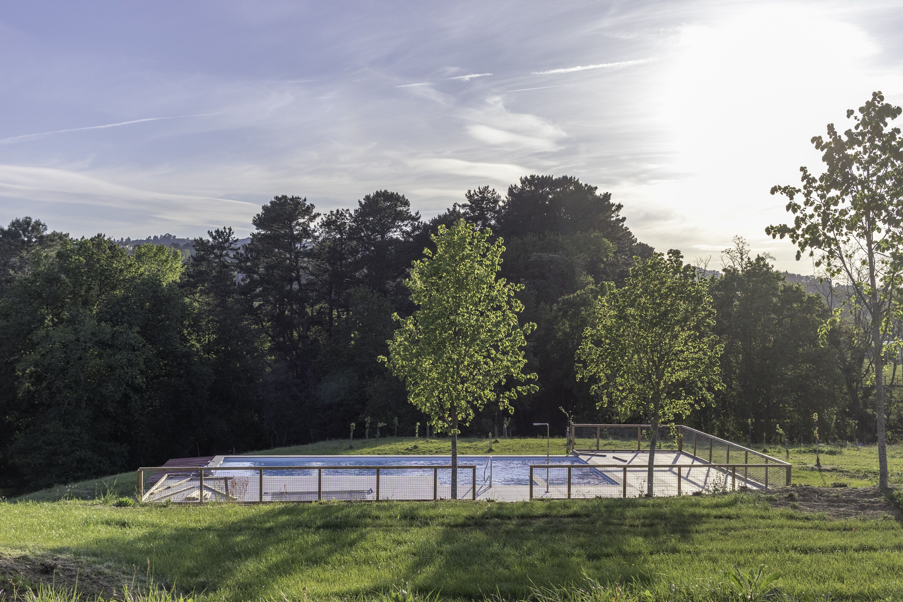 A swimming pool with a metal fence, surrounded by grass and trees.