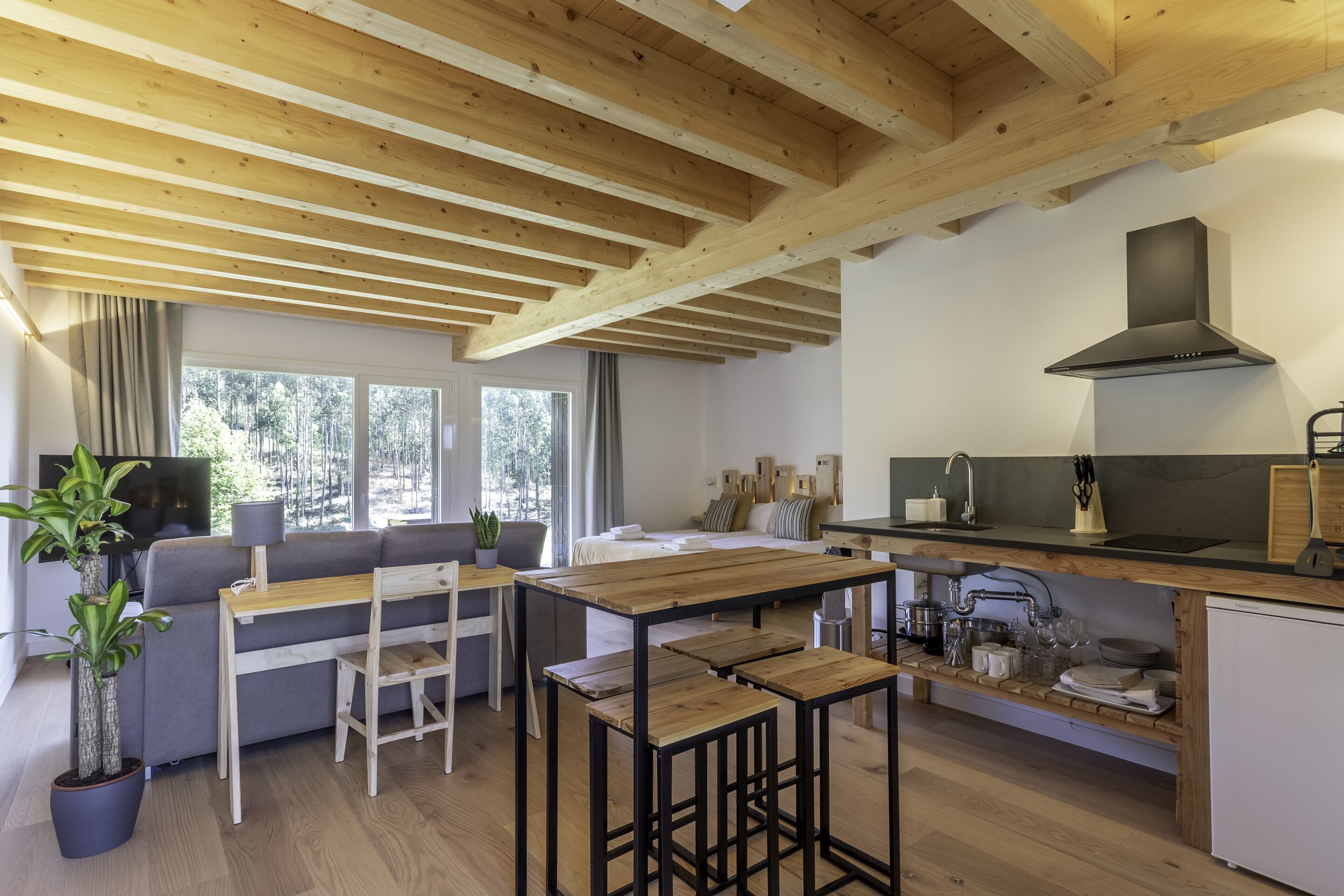 Una cocina moderna con vigas de madera, un comedor con mesa y sillas, y una sala de estar con sofá y televisor.