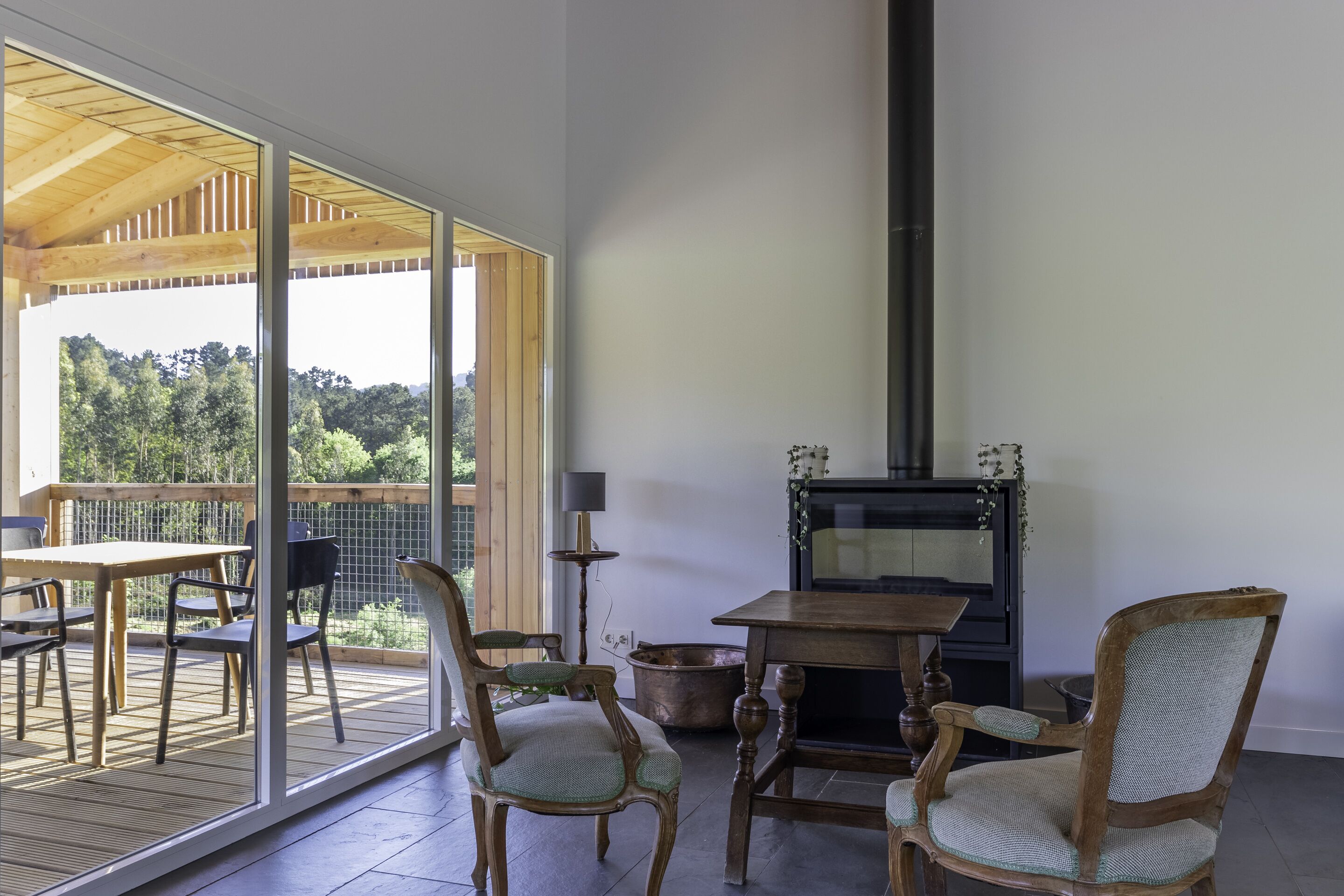 Una habitación con una mesa y sillas de madera, una chimenea y vistas a árboles a través de amplios ventanales.