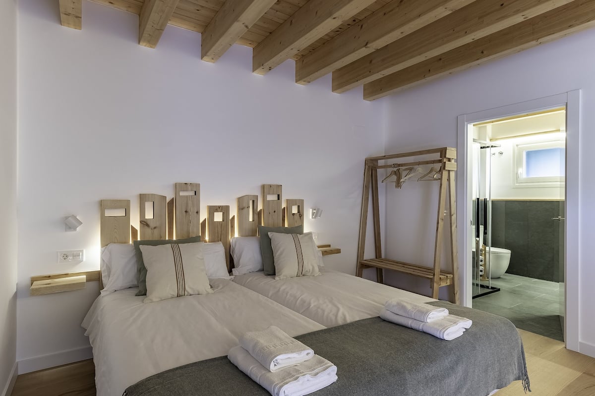 Uma cama de casal com cobertor cinza e duas toalhas, cabeceiras de madeira e um espelho.