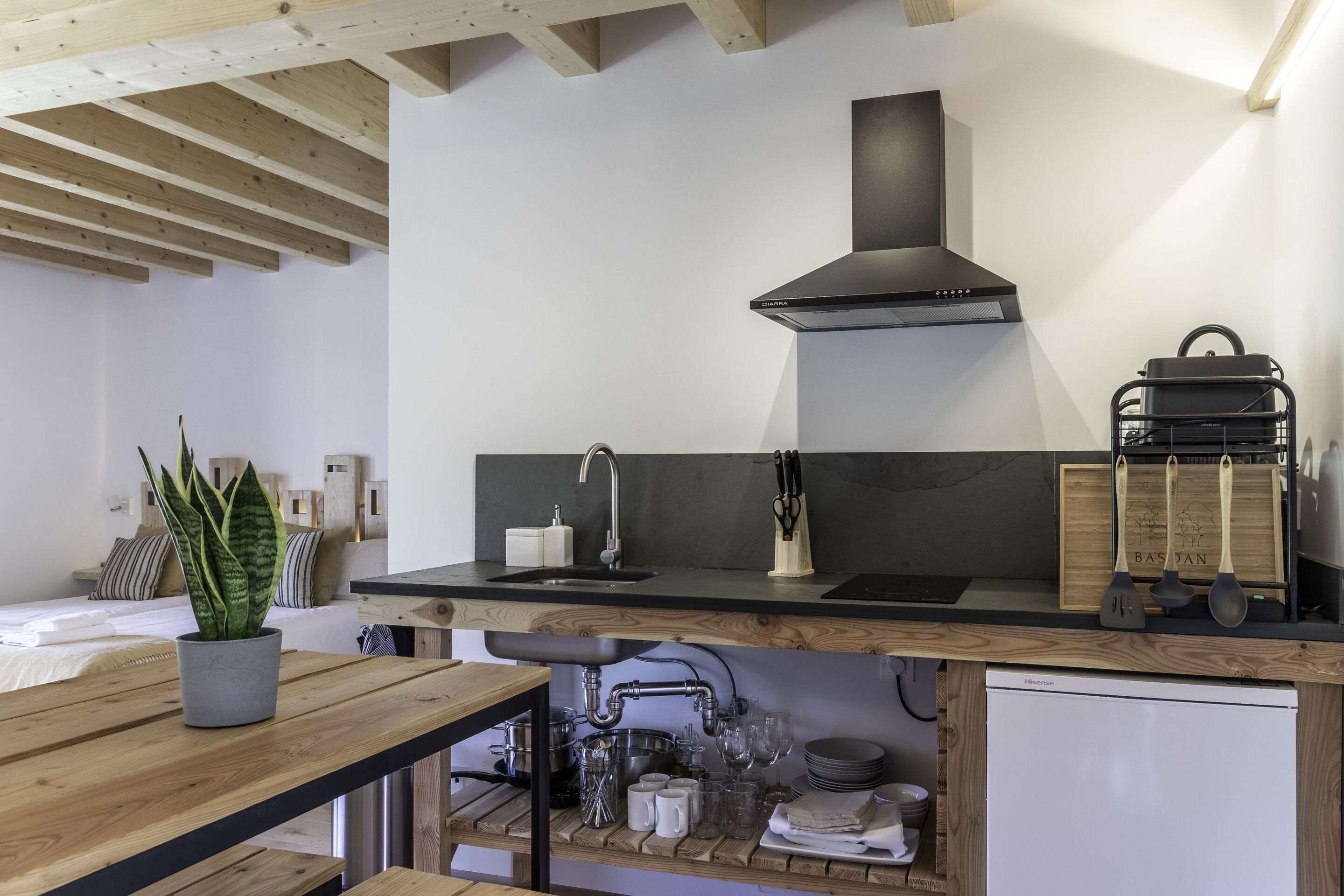 A modern kitchen with a wooden ceiling, a black range hood, a sink, and a dishwasher.