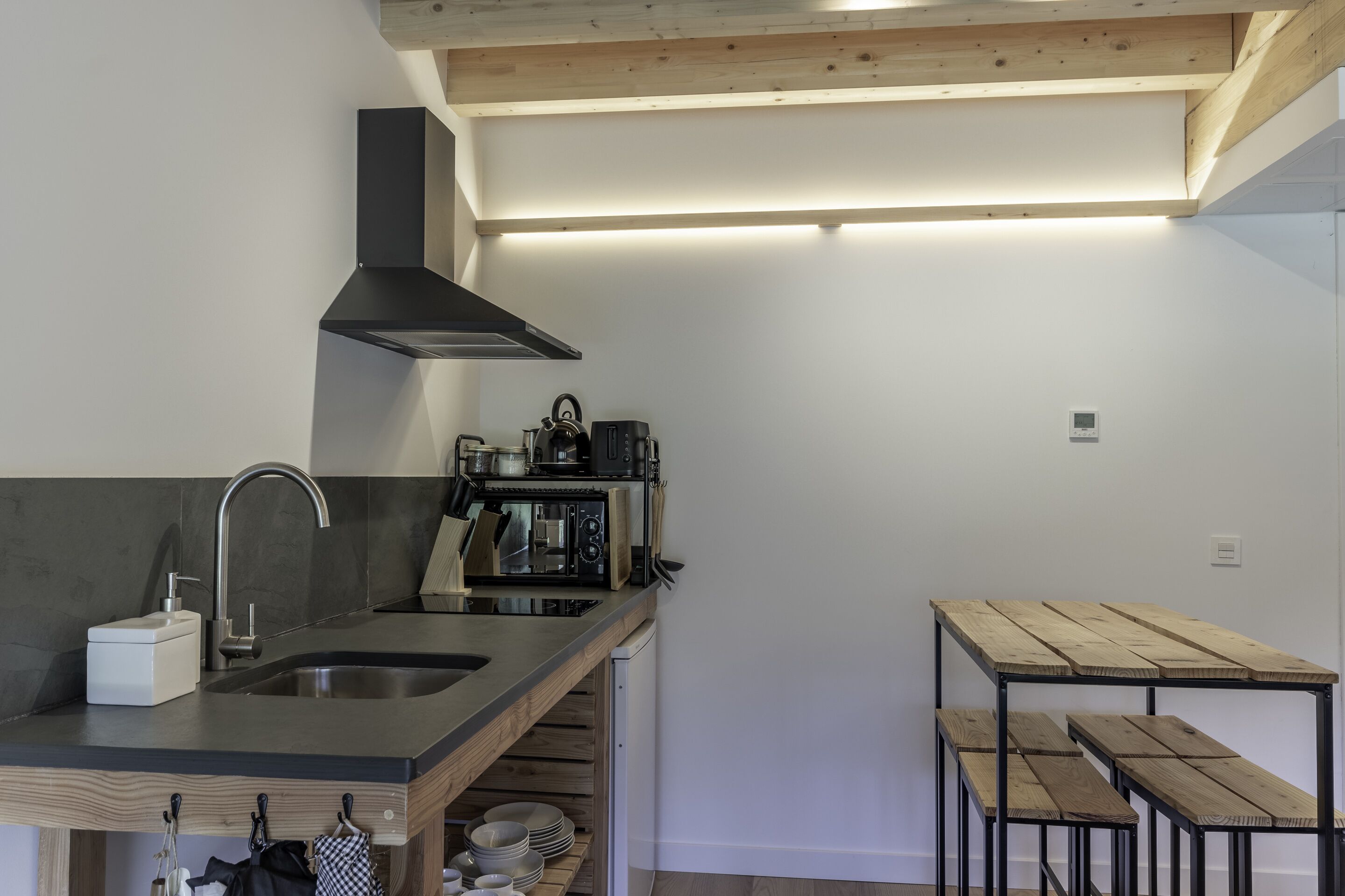 A modern kitchen with a built-in stove, sink, and wooden bench seating.